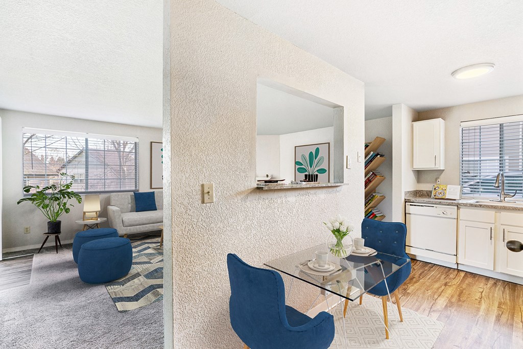 Living room and wood-floor kitchen divided by a textured wall with a looking window and staged with a breakfast table and chairs.at Capitol Crossing, Washington, 98501