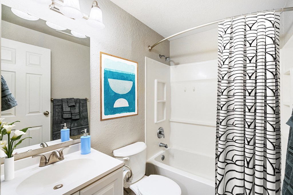 Bathroom with white sink top and below sink cabinets, mirror, toilet, shower with striped curtain.at Capitol Crossing, Olympia