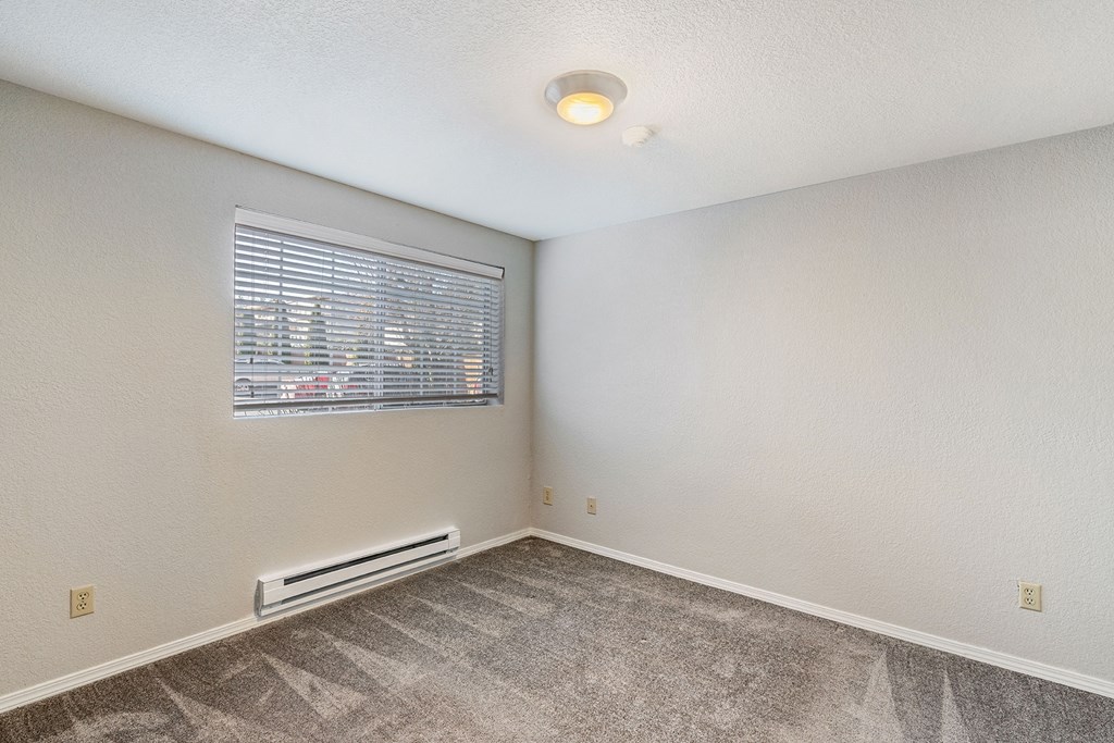 Bedroom with gray carpet, a window on the left wall, a heater below the window, and a light in the center of ceiling.at Capitol Crossing, Washington, 98501