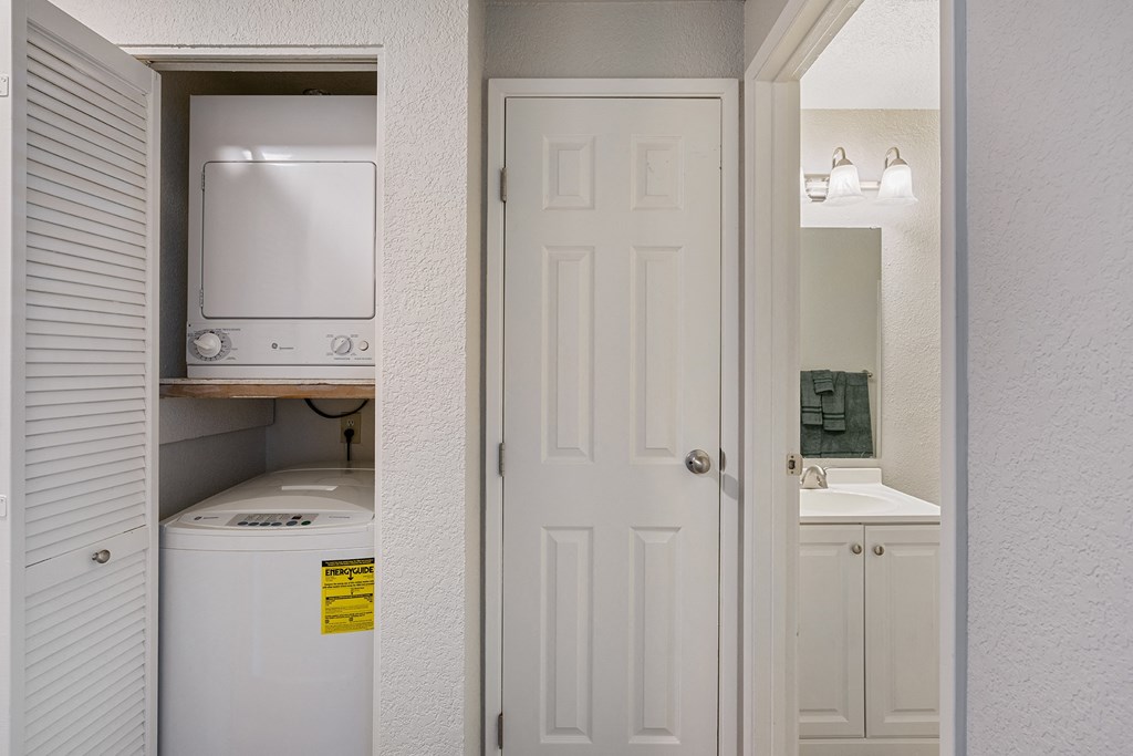 Stacked washer and dryer in shutter door closet to the left of a linen closet with bathroom on the right.at Capitol Crossing, Olympia, WA
