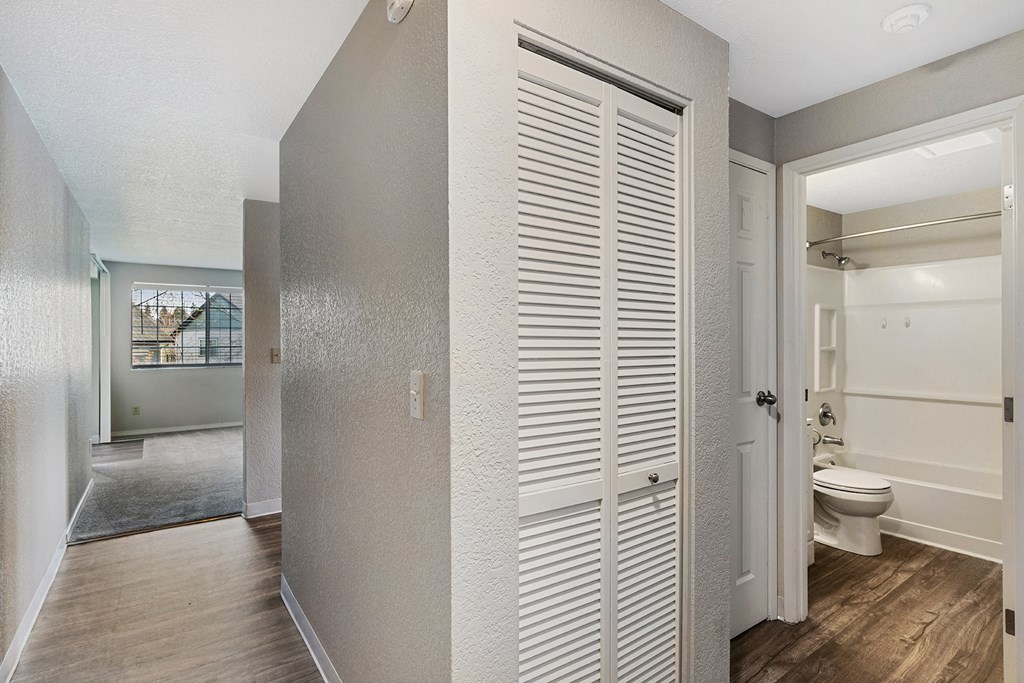 Wood floor hallway with access to living room and kitchen, shutter door closet, linen closet, and bathroom from left to right.at Capitol Crossing, Olympia, 98501