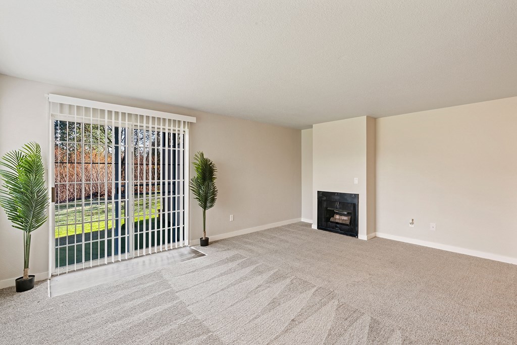 Living room with two plants beside sliding glass doors with panel blinds to grass lawn, and a gas fireplace on back right wall.at Capitol Crossing, Olympia, Washington