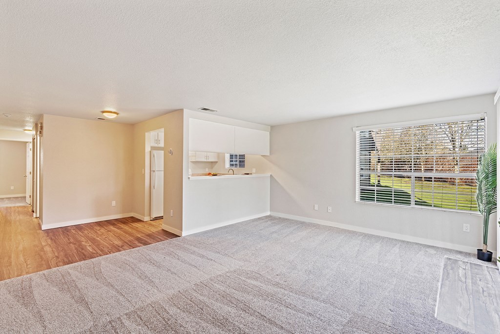 Spacious living room, window with a view of grass and trees, wood floor hallway past kitchen flowing to bedroom on the left.at Capitol Crossing, Olympia, WA