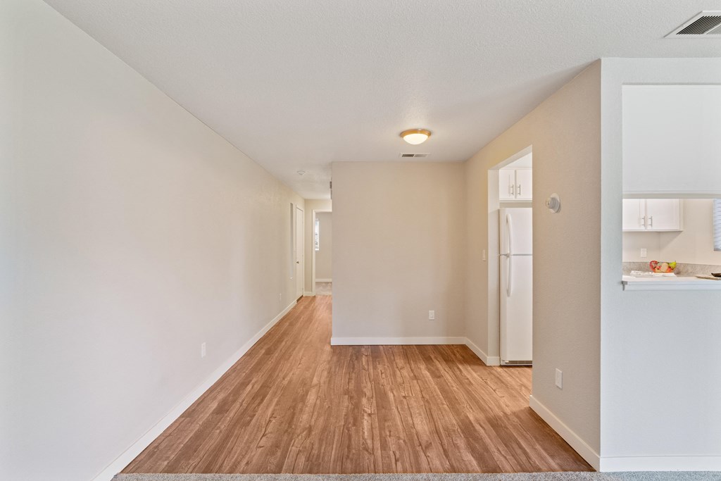 the living room and kitchen of an apartment with a hard wood floor and white walls