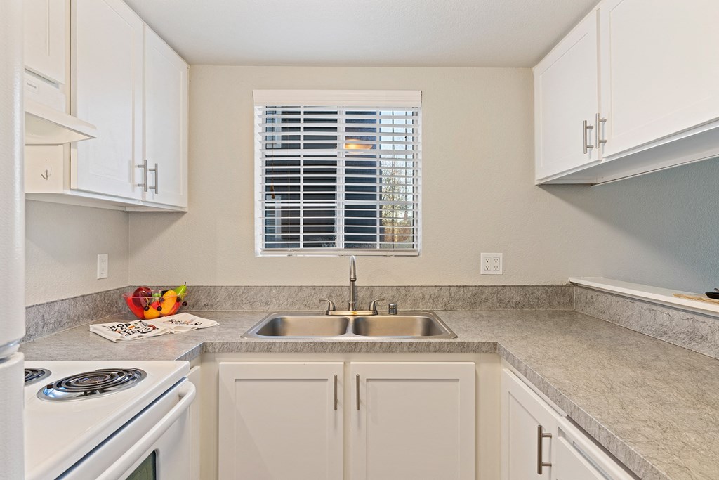 U-shaped kitchen with gray countertops, a window centered above stainless steel sink, and a bar-style counter on left.at Capitol Crossing, Washington, 98501