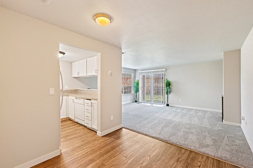 Wood floor kitchen and carpet living room divided by bar counter, sliding glass doors to outside, and window with blinds.at Capitol Crossing, Olympia
