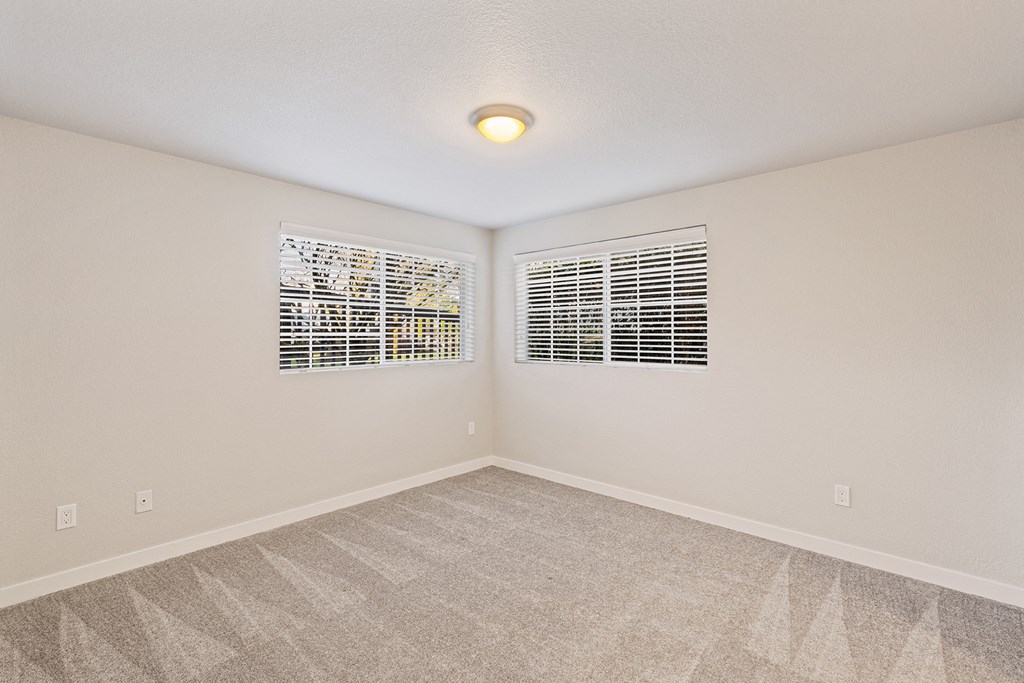 Bedroom corner, gray carpet, windows with white blinds on each wall, views of green trees.at Capitol Crossing, Olympia, Washington