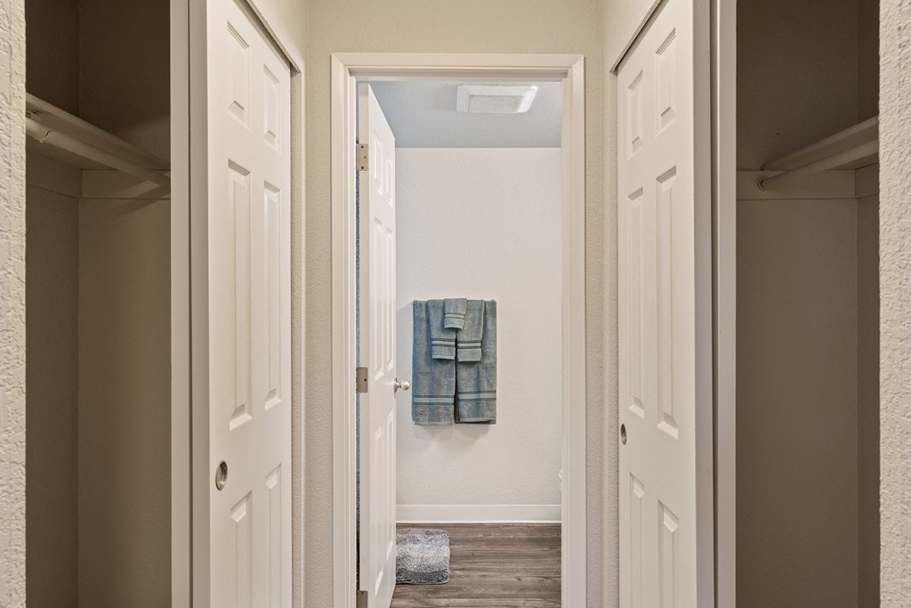Hallway with sliding door closets on either side leading to bathroom staged with bathmat and towelsat Capitol Crossing, Olympia, WA.