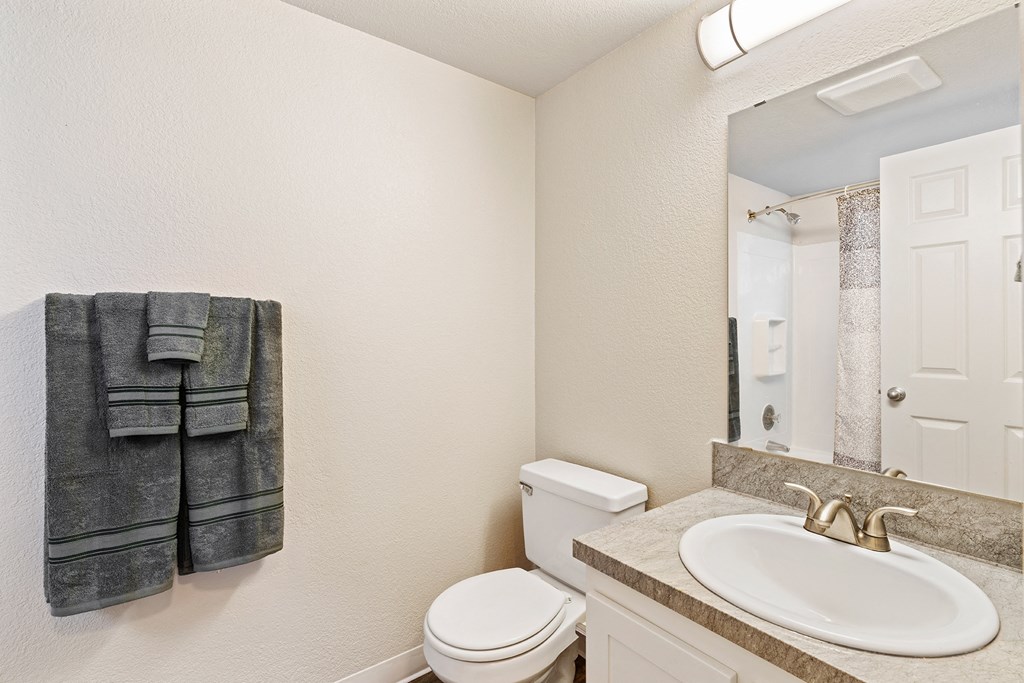 Bathroom with towel rack and staged gray towels, toilet, sink, under sink cabinets, and mirror with overhead lighting.at Capitol Crossing, Olympia, WA 98501