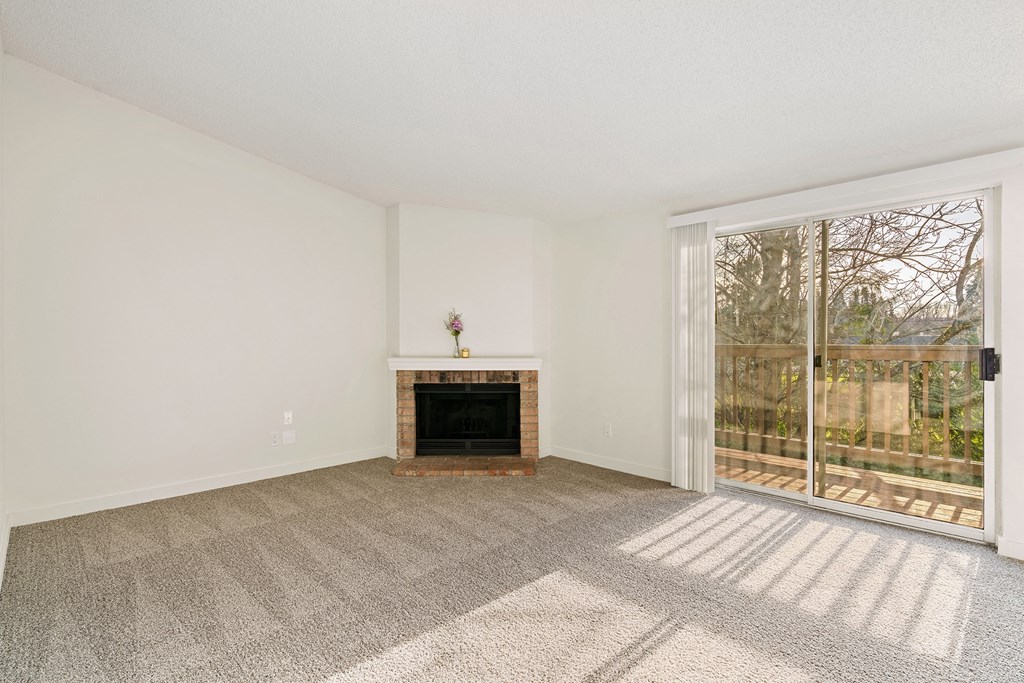 A large carpeted living room with white walls, a fireplace, and sliding glass doors to a private balcony with nature views. at Pointe East, Washington, 98424