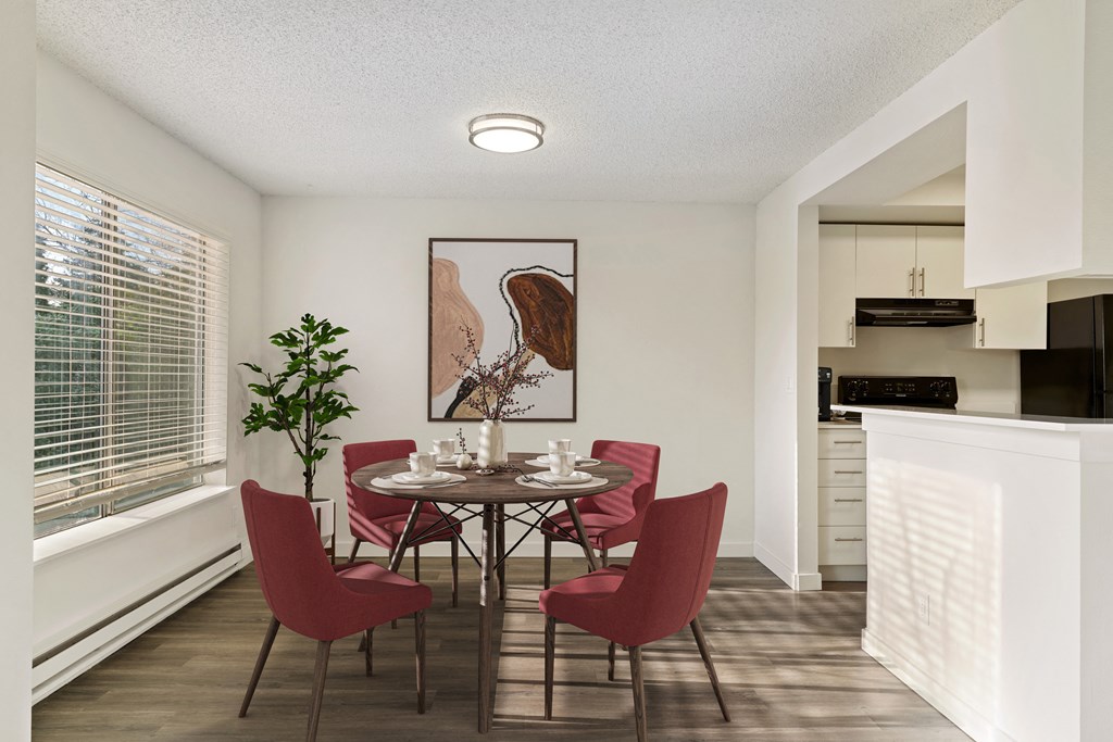 Dining room with white walls, hardwood flooring, a large window on the left wall, and the kitchen to the right. Staged with dining set. at Pointe East, Fife, WA