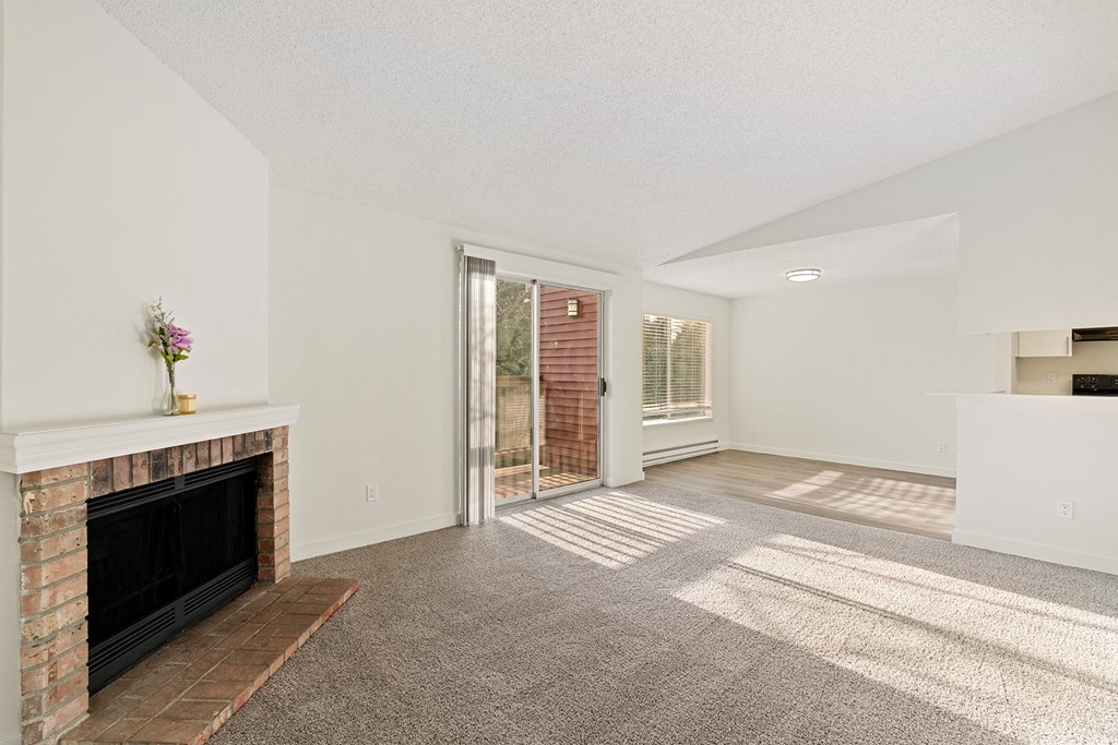 A Pointe East Apartments living room with carpet, a brick fireplace, access to a balcony, and a view of the dining room behind. at Pointe East, Washington, 98424
