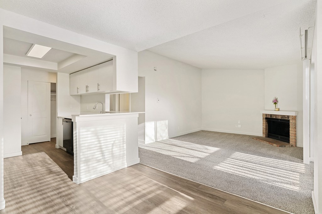 A kitchen with wood flooring, white cabinets, and a breakfast bar opens into a spacious carpeted living room. at Pointe East, Fife, WA