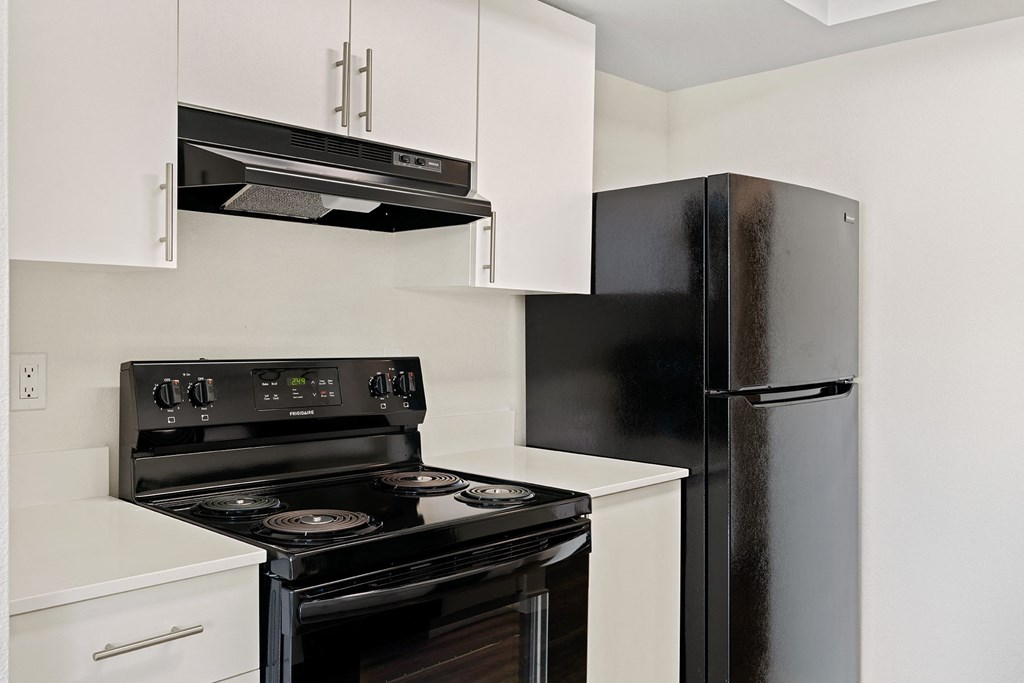 A close-up view of the kitchen with new white cabinets, an oven and stovetop, and a full-size fridge. at Pointe East, Washington, 98424