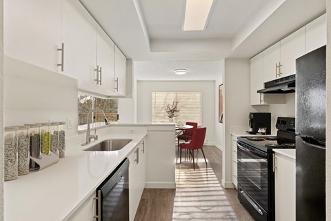 Bright kitchen with hardwood flooring, white top and bottom cabinets, and countertops. There is a dishwasher, sink, oven, stovetop, and fridge from left to right. at Pointe East, Washington, 98424
