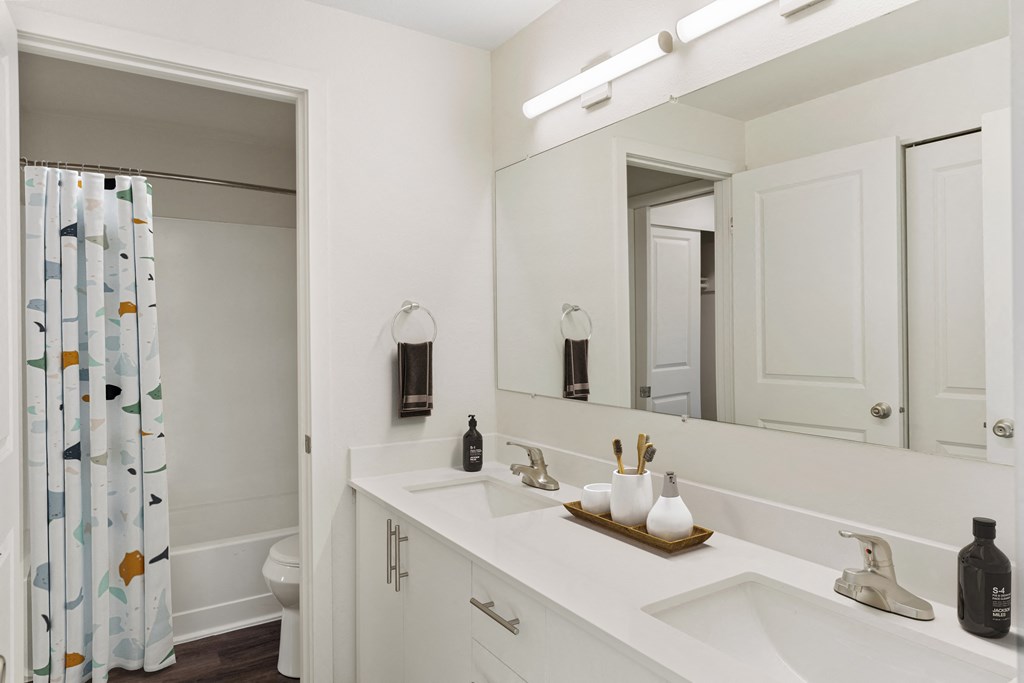 Full bathroom with a double sink vanity and cabinet storage, a large mirror, and a door to the shower and toilet. at Pointe East, Washington, 98424