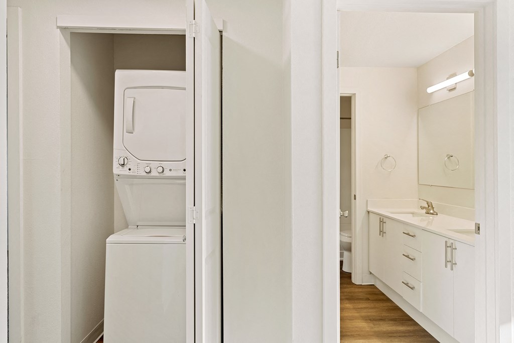 A closet with a white washer and dryer, and the full bathroom to the right with wood flooring. at Pointe East, Fife, WA, 98424