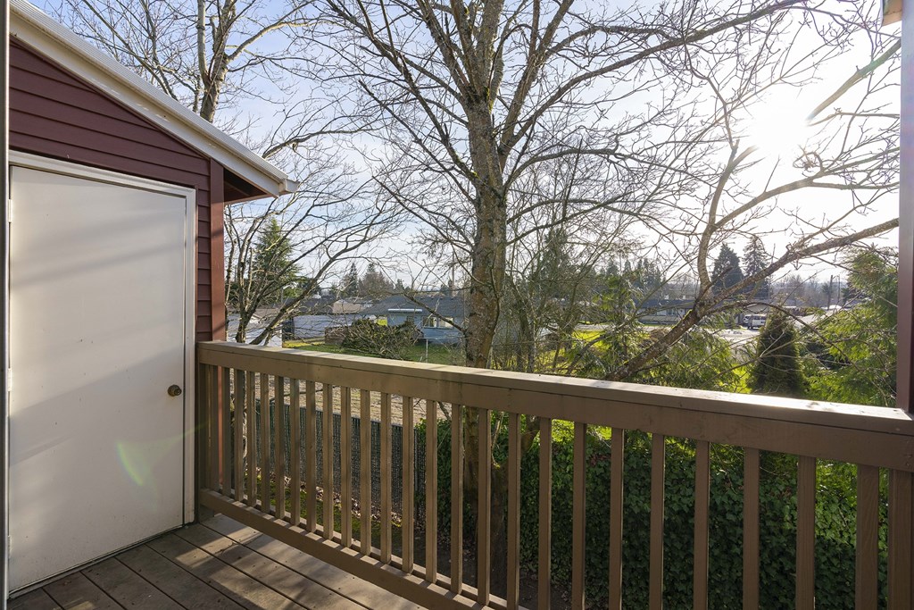 A private apartment balcony with a wood railing looks at trees, bushes, and a grass yard. at Pointe East, Fife, WA, 98424