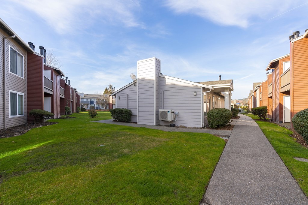 A paved pathway surrounded by green grass leads to apartments on a sunny blue sky day. at Pointe East, Washington, 98424