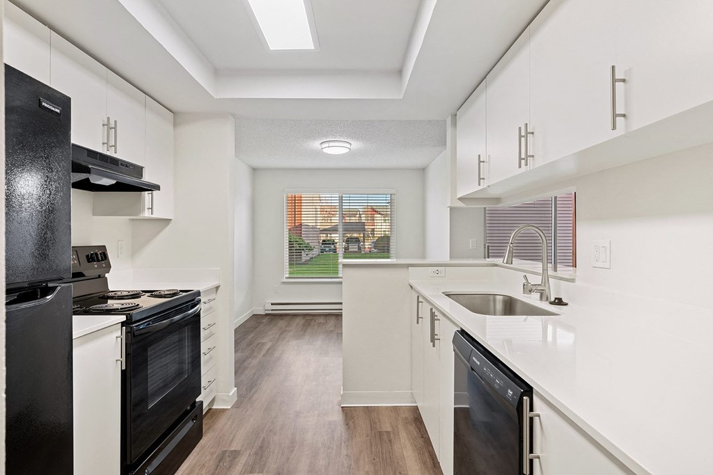 A galley-style kitchen with white countertops and cabinets looks into the dining room with a large window and a view of a grass lawn. at Pointe East, Washington