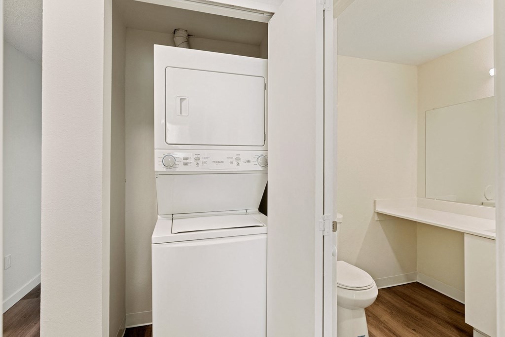 A closet with a white washer and dryer stacked and access to the bathroom on the right. at Pointe East, Washington, 98424