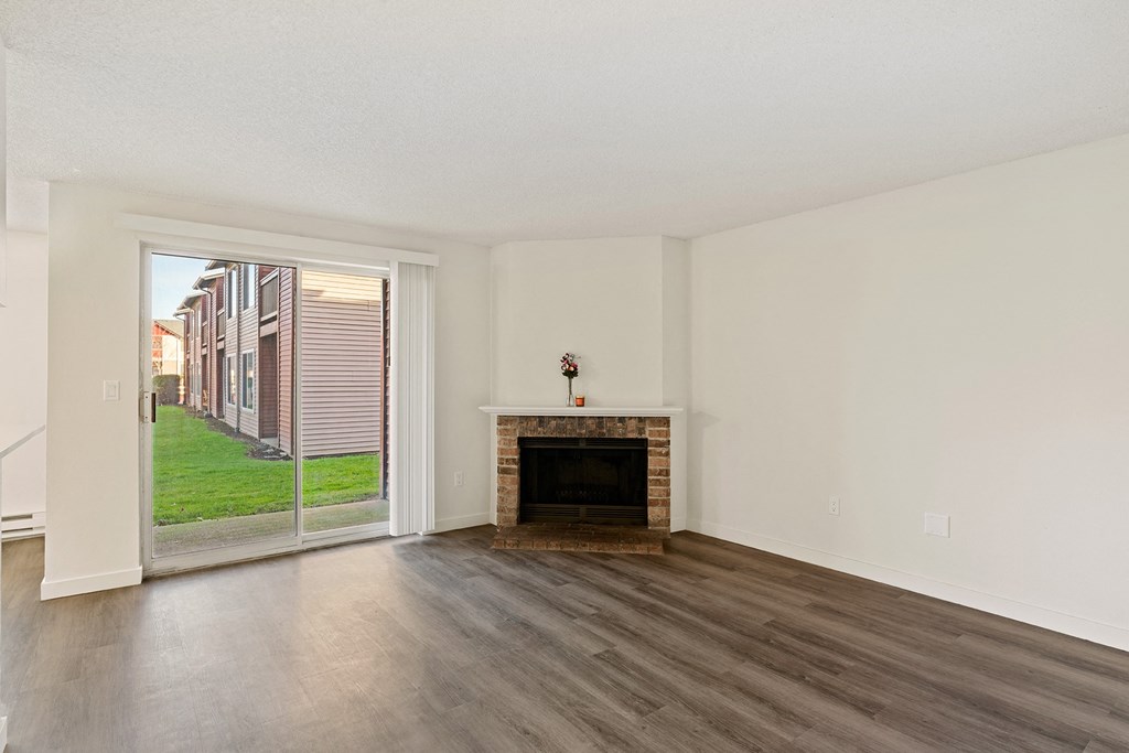 A living room with wood flooring, a brick fireplace and sliding glass doors. at Pointe East, Fife, Washington