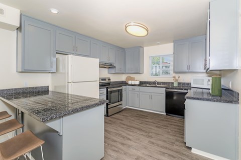 A kitchen with a granite counter top and grey cabinets.