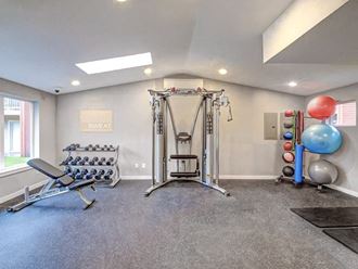 The apartment gym has a weight bench, free weights, a large cable machine, medicine and yoga balls, and black workout mats at Pointe East, Fife, WA