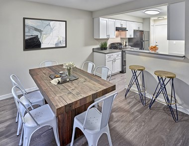 Spacious dining room that flows into the kitchen. Staged with a dining table, bar stools, and wall art.