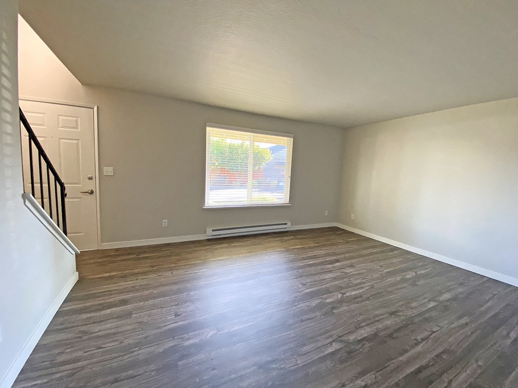 Spacious living room with large window, wood-style flooring, front door, and stairs to the right.at Quilceda Gardens, Washington