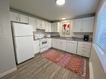 L-shaped kitchen with top and bottom cabinet storage, gray countertops, white appliances, and a large window on the right wall. - Photo Gallery 7