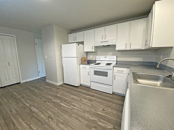L-shaped kitchen with white appliances, top and bottom cabinets, wood-like flooring, and closet. - Photo Gallery 14