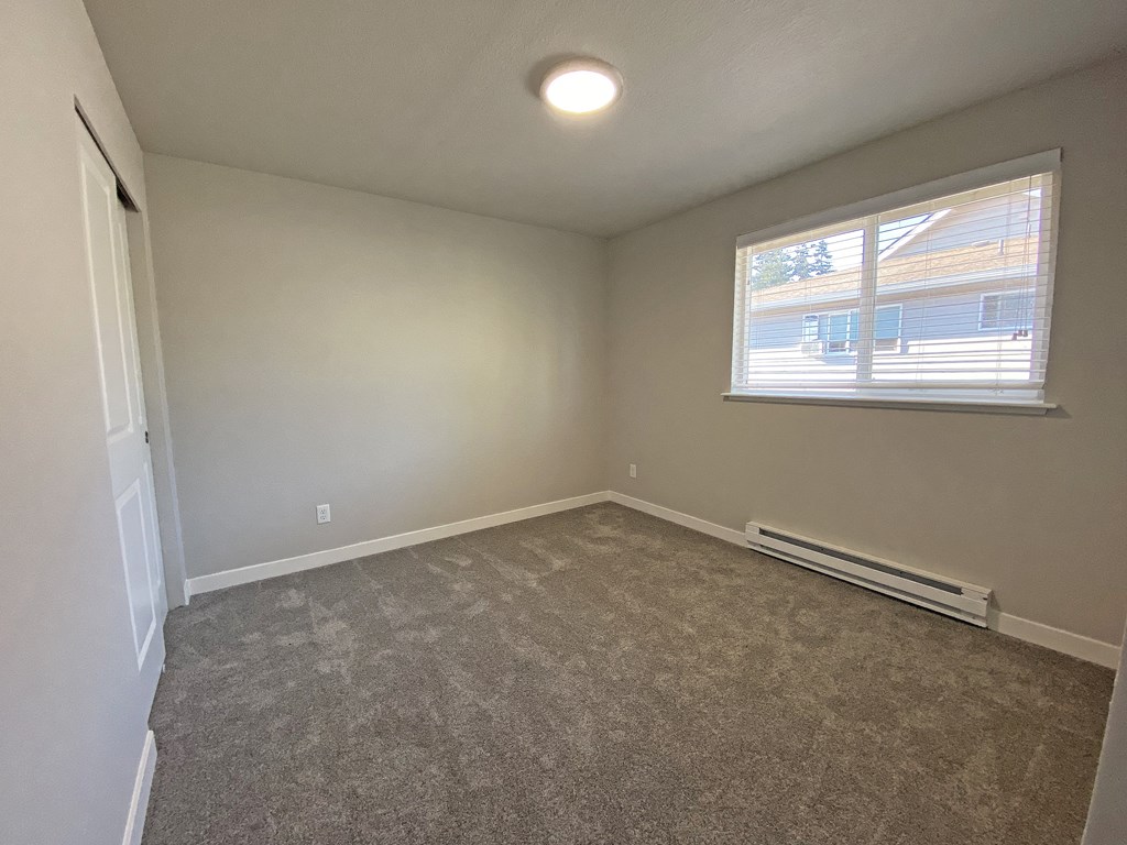 Bedroom with gray carpets, large closet on the left opposite window with white blinds and heater below.at Quilceda Gardens, Marysville, WA 98270