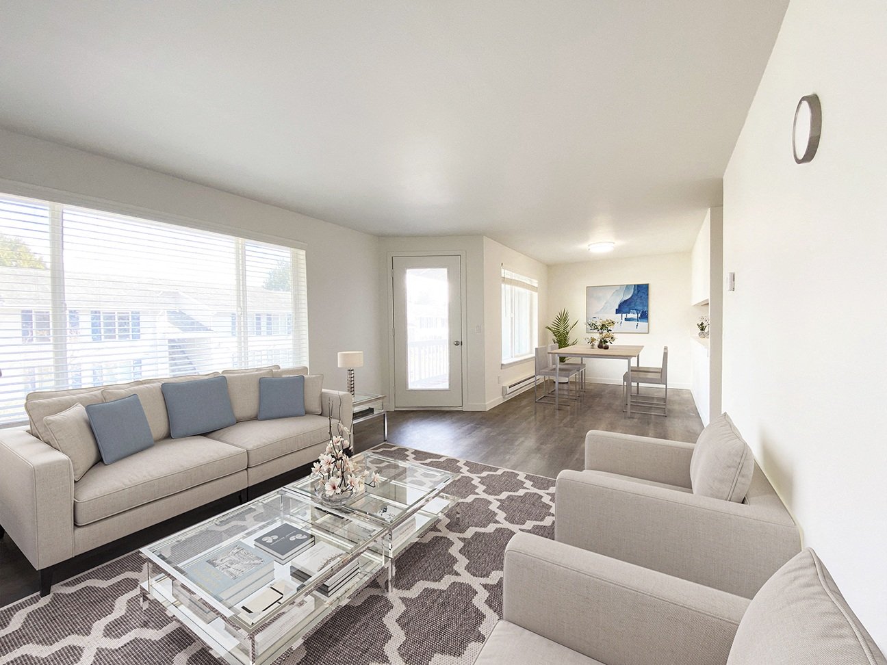 Bright spacious living room with three huge windows, a door to the private balcony and the dining room past the door. Staged with a couch, coffee table, 2 chairs and a rug.