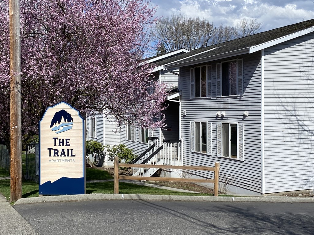 the Trail Apartments sign in front of a white building with a cherry tree in the foreground.at The Trail, Washington