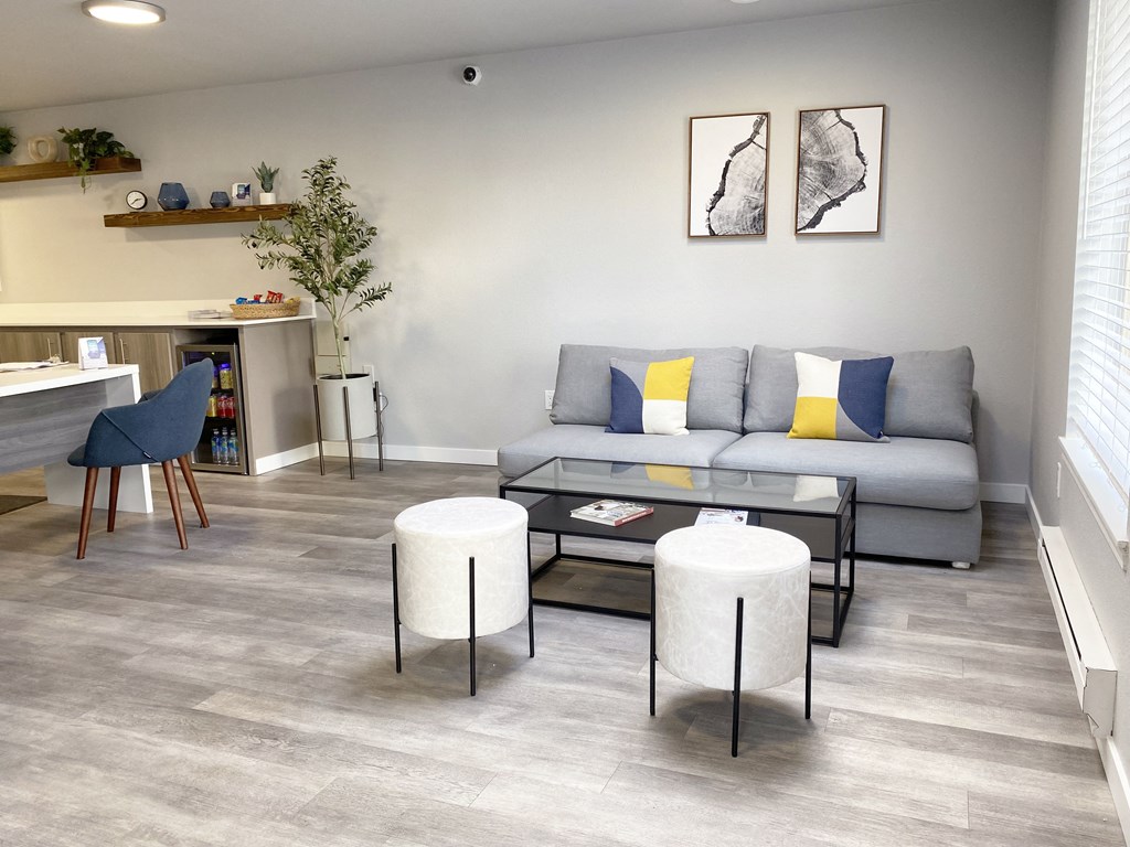 The Trail Apartments lobby with a gray couch, a coffee table, ottoman seating, a mini fridge with drinks and a long table with snacks.at The Trail, Snohomish, 98290