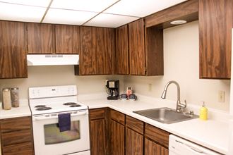 L shaped kitchen with brown cabinets, white appliances and stainless steel sink.at The Lakes Apartments, Moses Lake Washington