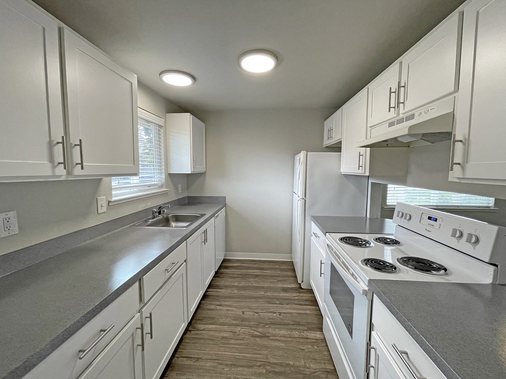 Kitchen with white cabinets, full-size fridge, sink, stovetop, oven, dishwasher, w/ opening looking into living room.at Quilceda Gardens, Marysville