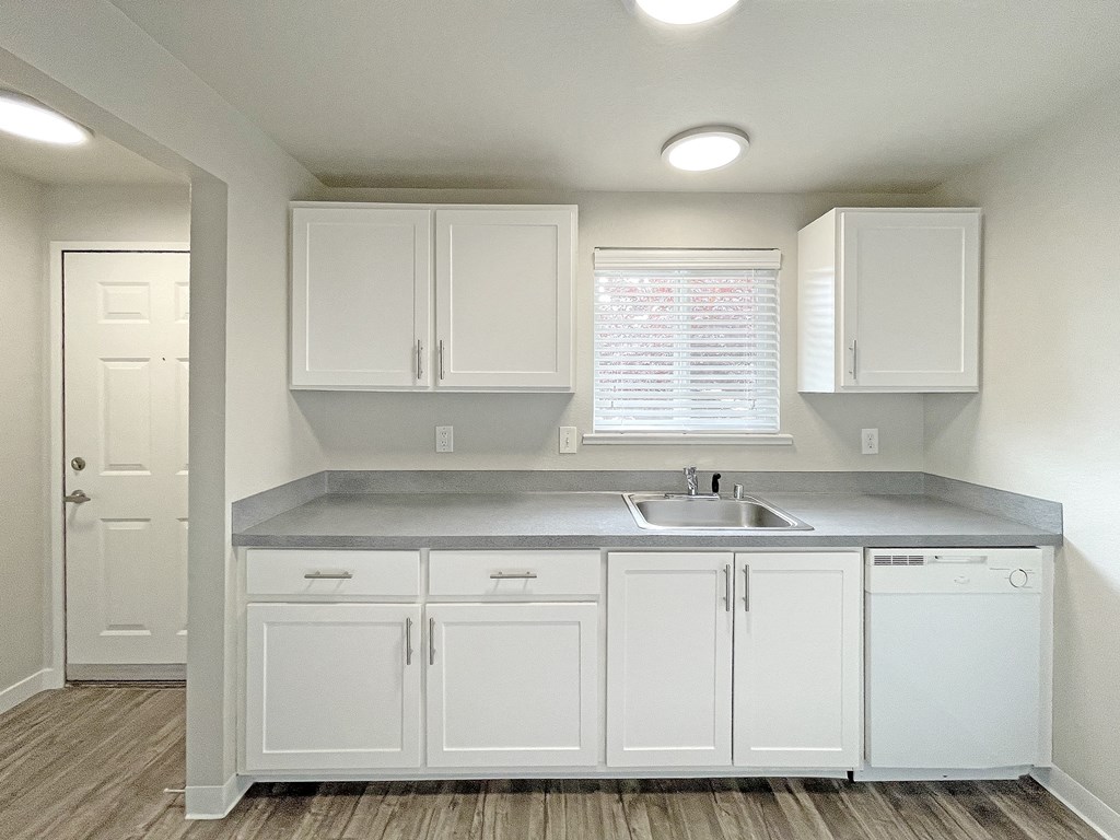 Light-filled kitchen with white cabinets and appliances, a window above the sink, and wood-like flooring.at Quilceda Gardens, Washington