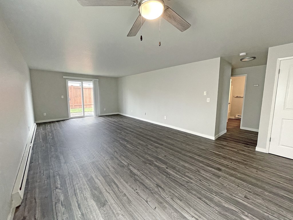 Open layout living room with ceiling fan and sliding glass doors on the back wall to private fenced-in patio.at Quilceda Gardens, Washington, 98270