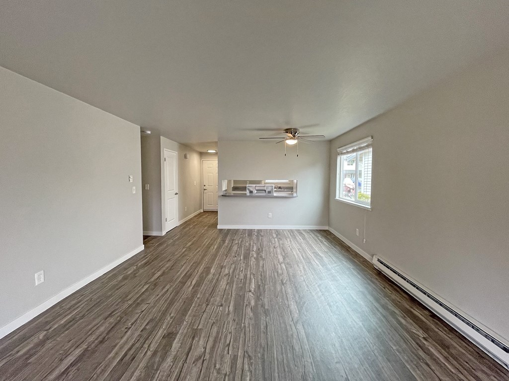 Spacious living room with dining area looking into kitchen with wood-like flooring and oversized window on the right.at Quilceda Gardens, Marysville, WA