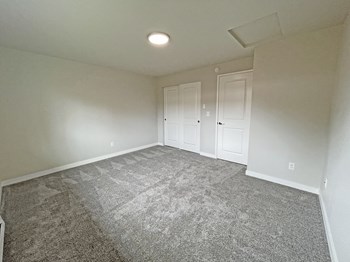 Large carpeted bedroom with double sliding door closet on the back wall next to the bedroom door. - Photo Gallery 23