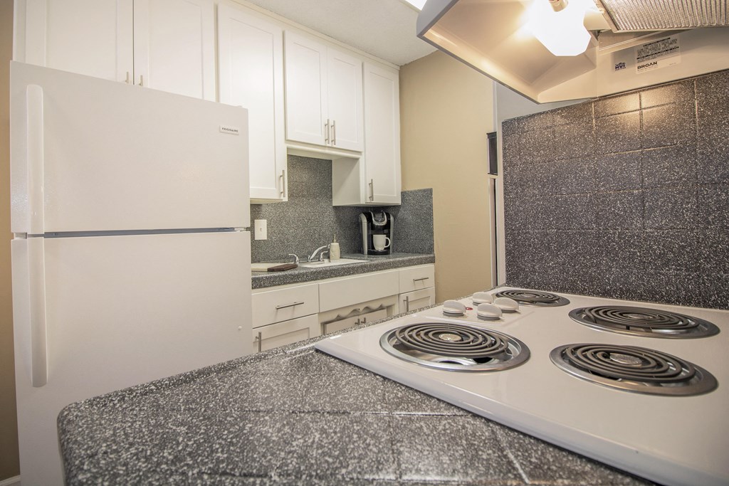 Galley kitchen with new white cabinets and gray faux granite countertops, with dining area visible in the distance  at Woodland Village Apartments , Woodland, CA 95695