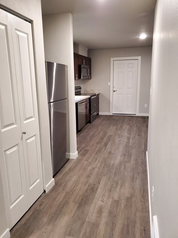 Hallway with double door closet opens into the kitchen with a full-size fridge, sink, dishwasher, flat stovetop, and microwave. - Photo Gallery 13