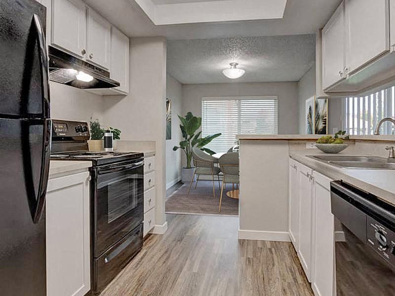 A kitchen with a full-size fridge, oven, stovetop, double bowl sink, and dishwasher. White top and bottom cabinets and a breakfast bar. at Pointe East, Fife, Washington