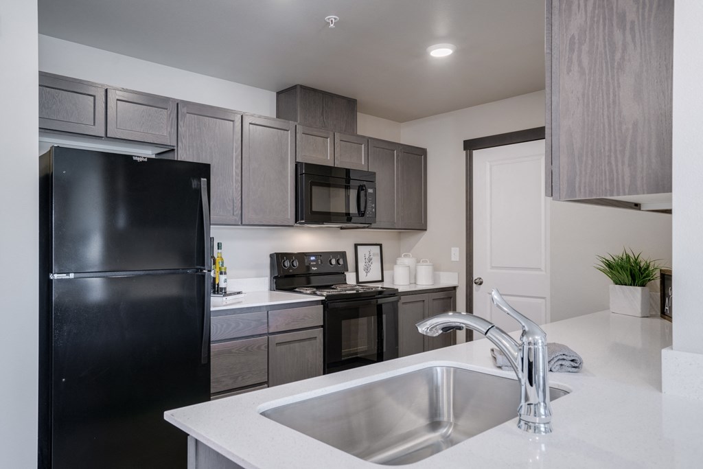 Kitchen with white countertops and grey cabinets. Kitchen has black fridge, black stove and oven, black microwave and stainless steel sink. at Altitude, East Wenatchee, WA, 98802