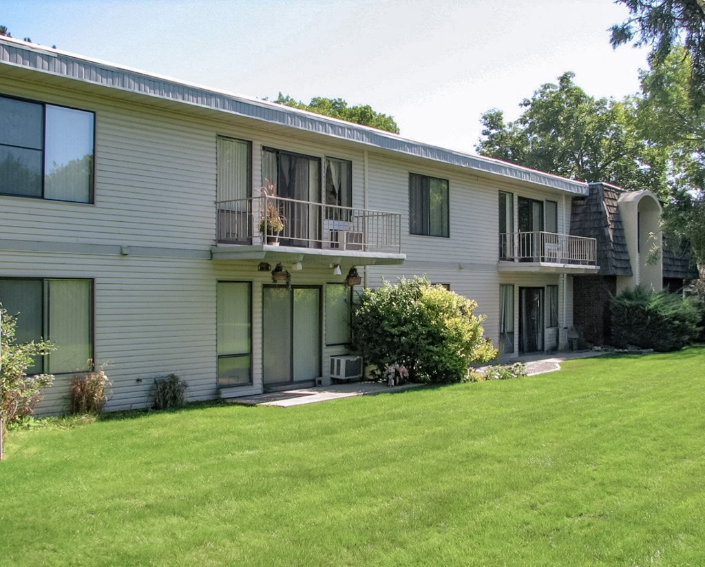 Exterior apartments with large windows, balconies, large patios surrounded by manicured grass, landscaping, and trees behind.at Laurel Park, Idaho