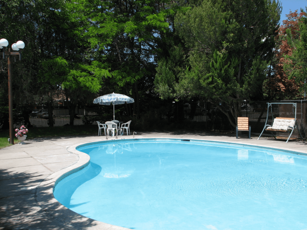 Swimming pool with umbrella seating, swing bench, surrounded by manicured lawn and large green trees.at Laurel Park, Twin Falls