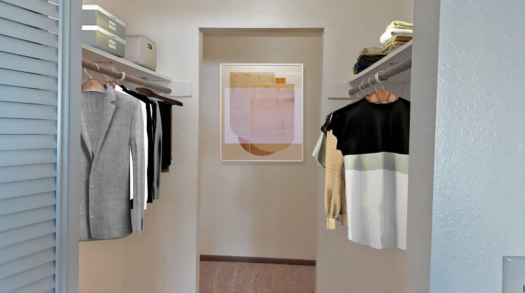 Walk-in closet, carpeted, with shelving, closet rod, staged with clothes on hangers, framed art.at Laurel Park, Twin Falls, ID