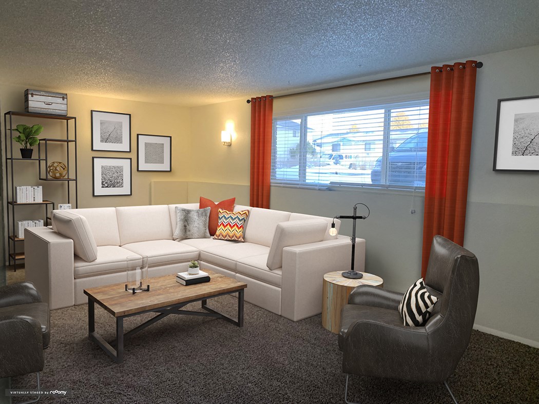 Large carpeted living room with oversized window and staged with l-shaped couch, 2 chairs, coffee table, wall art.